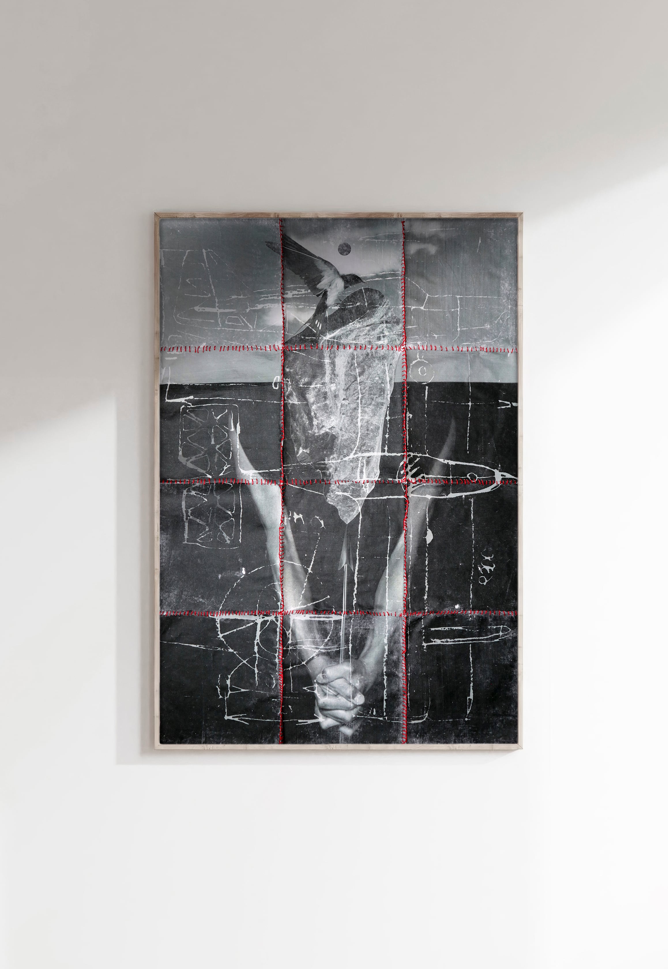 Framed collage divided into a grid by red lines, showing a monochrome photographic figure with an animal-skull-like silhouette over a gridded ledger-paper background