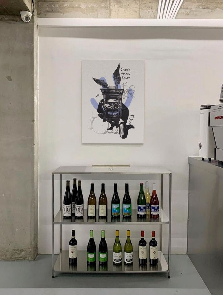 Print reading "Sorry, no art today" hanging above a wine shelf and espresso machine